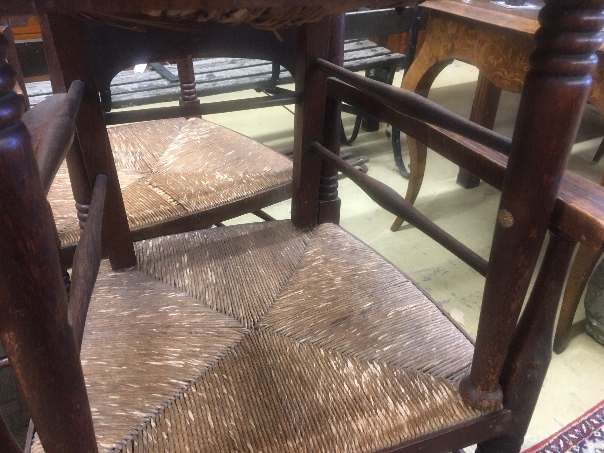 A set of six Arts & Crafts oak chairs, including a pair of carvers, in the Glasgow School manner by William Birch, High Wycombe, with shaped panels backs, ring turned frames and rush seats, carvers W.58cm D.54cm H.109cm